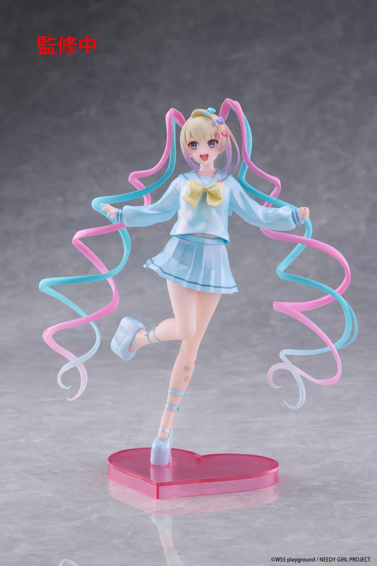 Needy Girl Overdose OMGKawaiiAngel Coreful Figure featuring a blonde-haired anime girl with blue eyes, long pink and blue twin-tails, a pastel-blue sailor-style outfit, yellow bow, and matching shoes posed on a pink heart-shaped base.