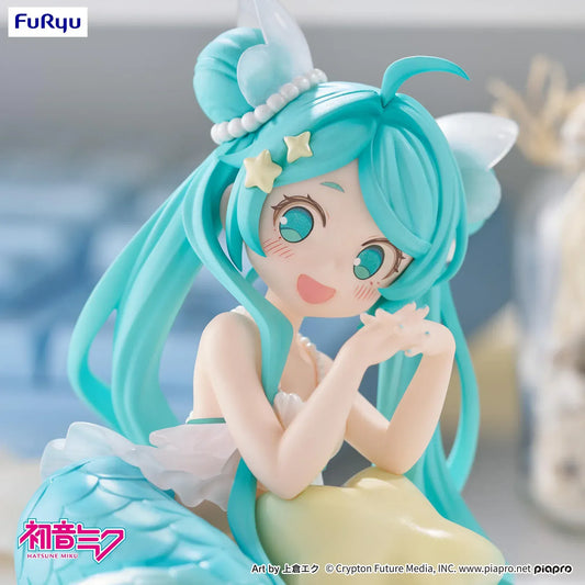 Pastel mermaid Hatsune Miku desktop fairy figure lounging on a star cushion with a mint-green tail and twin-tails, displayed on a desk with seashells and a keyboard in the background.