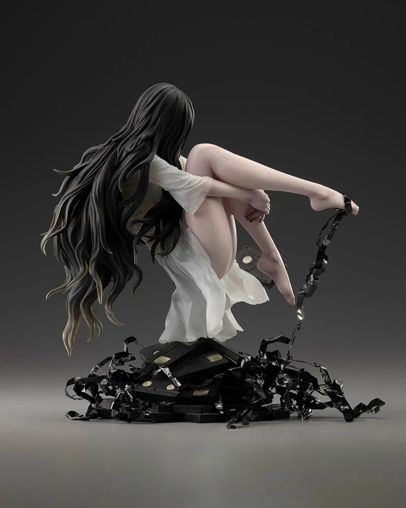 Sadako BISHOUJO Sadako 1/7 Scale Figure (Rerelease) featuring a long black-haired horror character wearing a flowing white dress, seated above a pile of VHS tapes with tangled black film ribbons.