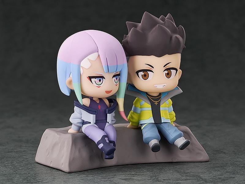 Cyberpunk: Edgerunners Qset+ David & Lucy To The Moon Figure (Rerelease) featuring chibi-style David Martinez with spiky black hair and a yellow jacket sitting beside Lucy Kushinada with pastel-colored hair and a purple futuristic outfit on a shared display base.
