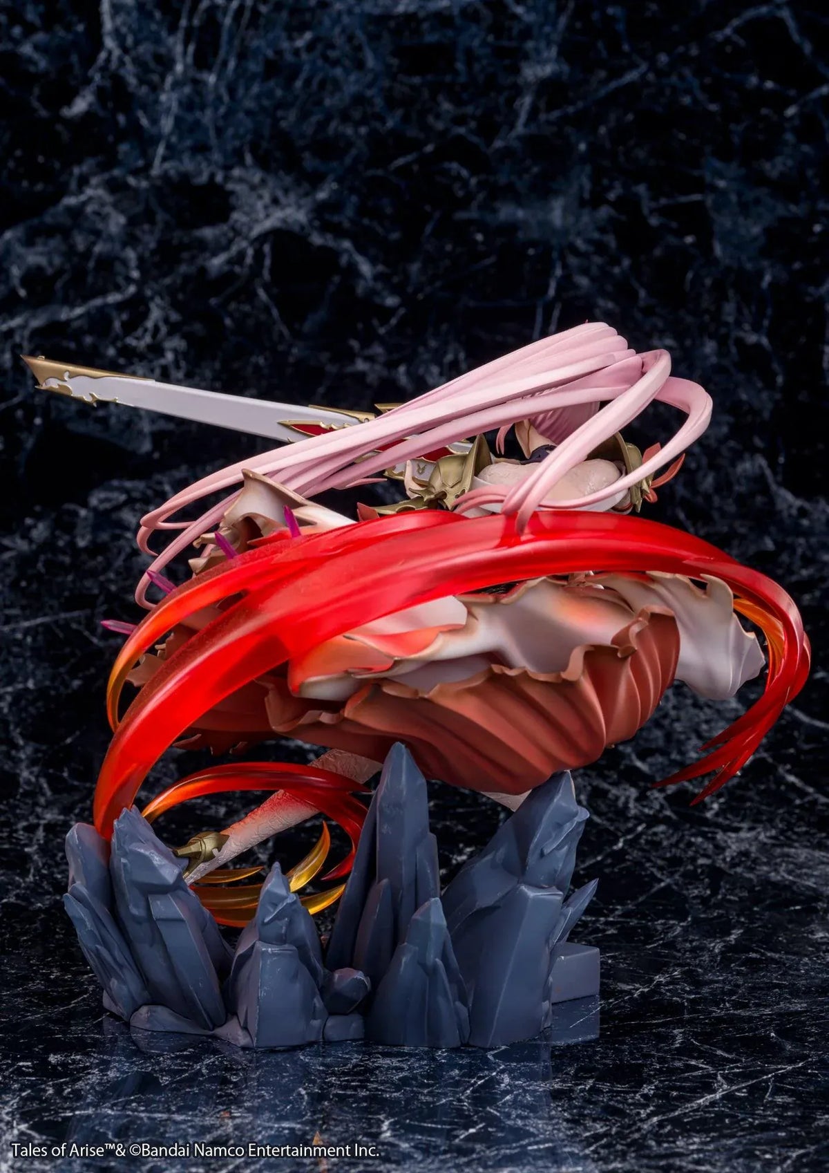 Tales of Arise Shionne 1/7 Scale Figure featuring a pink-haired anime character with blue eyes, an ornate white battle dress, gold armor, and lace stockings, aiming a detailed rifle while suspended in a dynamic pose surrounded by translucent red and orange effects on a rocky display base.