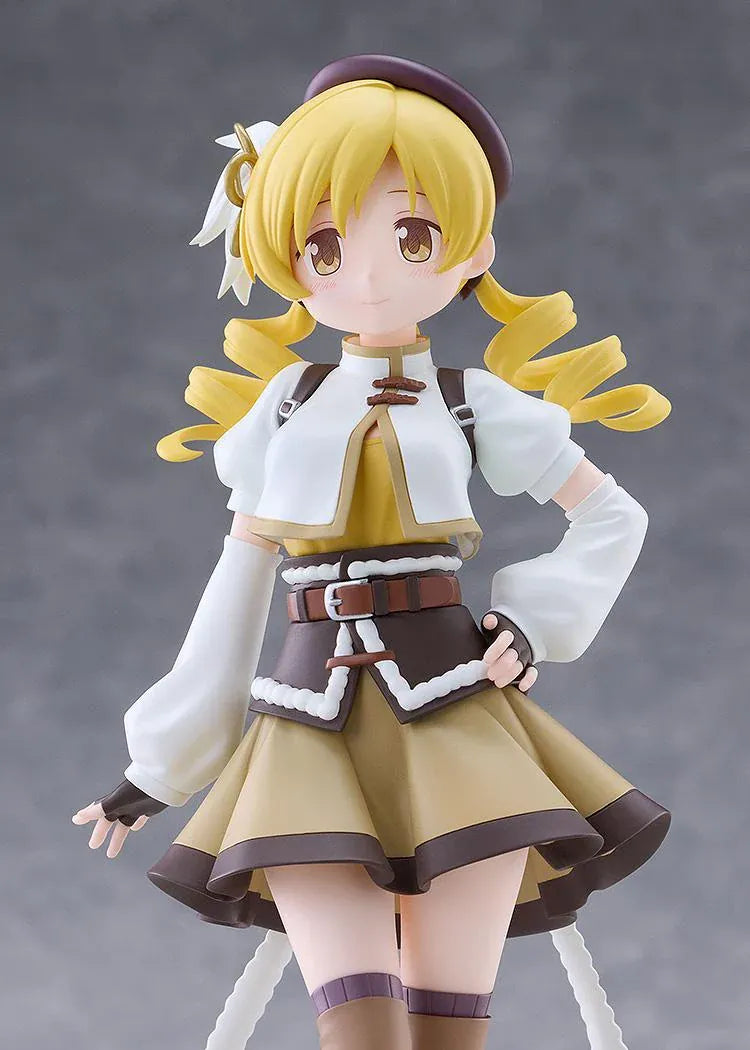 Mami Tomoe figure with blonde spiral curls, a brown hat, white and gold outfit, and tall brown boots, posing with one hand on her hip.