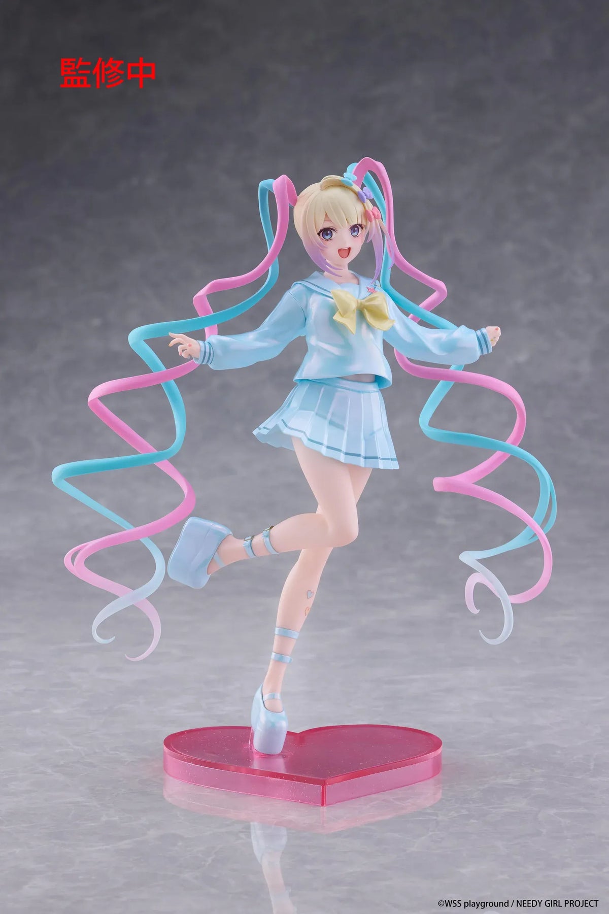 Needy Girl Overdose OMGKawaiiAngel Coreful Figure featuring a blonde-haired anime girl with blue eyes, long pink and blue twin-tails, a pastel-blue sailor-style outfit, yellow bow, and matching shoes posed on a pink heart-shaped base.