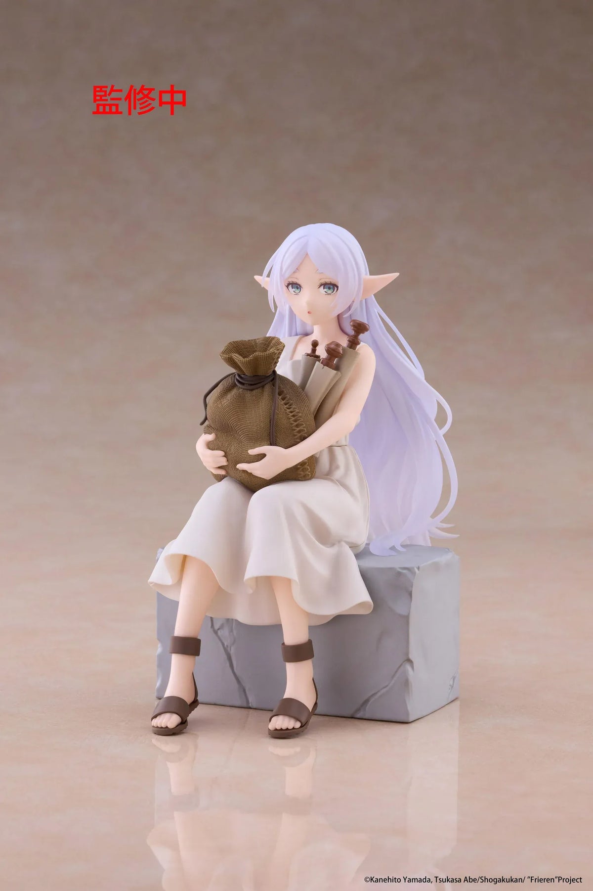 Desktop Cute Frieren In Training Ver. figure seated on a gray stone block, wearing a cream dress and brown sandals while holding a sack beside rolled scrolls.
