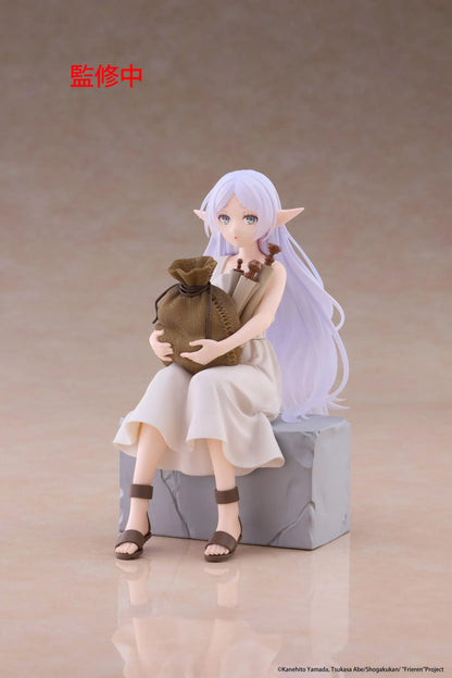 Desktop Cute Frieren In Training Ver. figure seated on a gray stone block, wearing a cream dress and brown sandals while holding a sack beside rolled scrolls.
