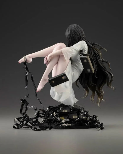Sadako BISHOUJO Sadako 1/7 Scale Figure (Rerelease) featuring a long black-haired horror character wearing a flowing white dress, seated above a pile of VHS tapes with tangled black film ribbons.