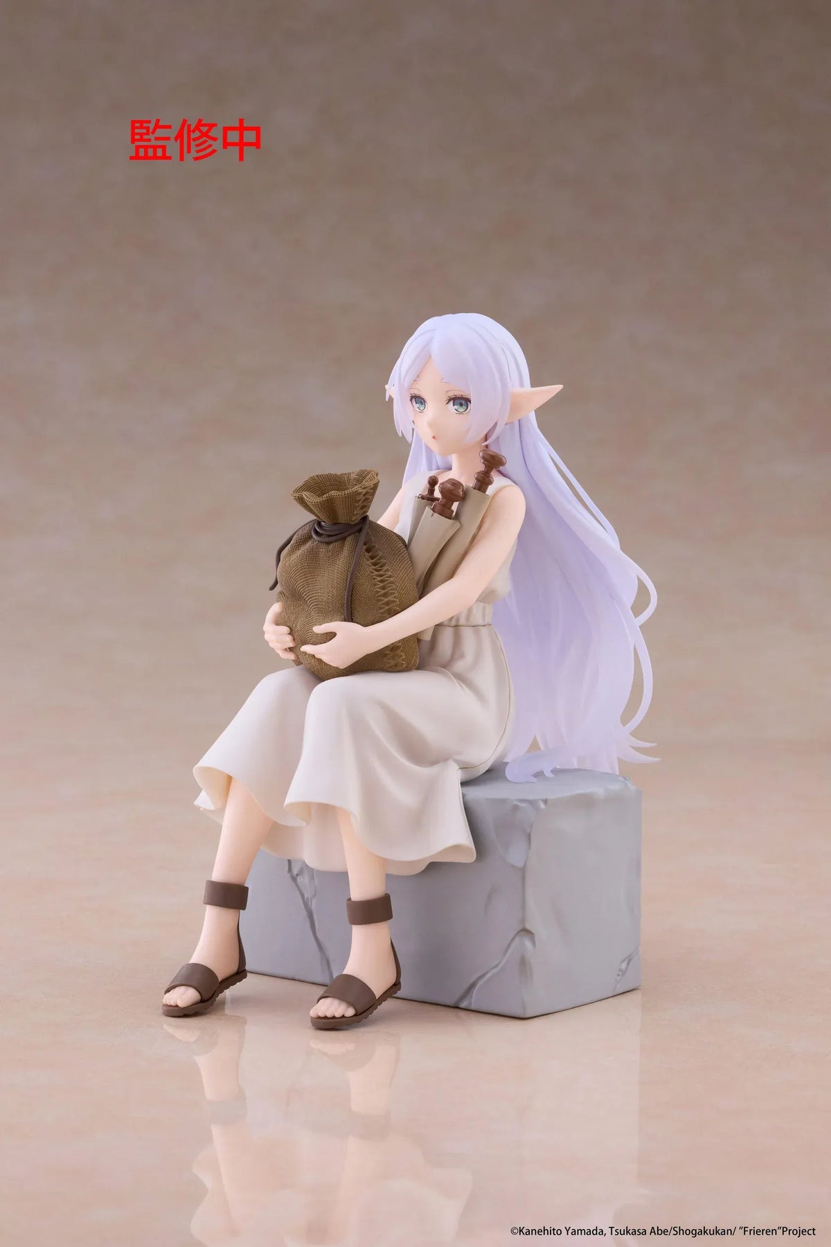Desktop Cute Frieren In Training Ver. figure seated on a gray stone block, wearing a cream dress and brown sandals while holding a sack beside rolled scrolls.