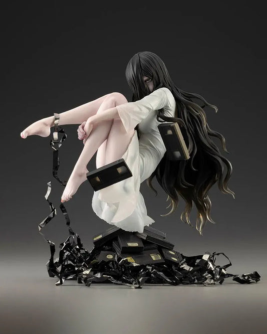 Sadako BISHOUJO Sadako 1/7 Scale Figure (Rerelease) featuring a long black-haired horror character wearing a flowing white dress, seated above a pile of VHS tapes with tangled black film ribbons.