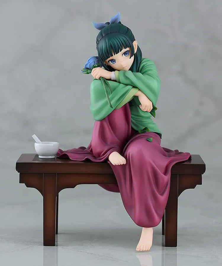 Maomao 1/7 scale figure seated barefoot on a wooden bench, wearing a green top and plum skirt, holding a blue flower beside a mortar and pestle.