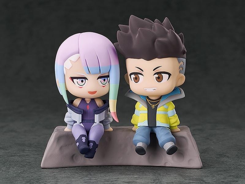 Cyberpunk: Edgerunners Qset+ David & Lucy To The Moon Figure (Rerelease) featuring chibi-style David Martinez with spiky black hair and a yellow jacket sitting beside Lucy Kushinada with pastel-colored hair and a purple futuristic outfit on a shared display base.