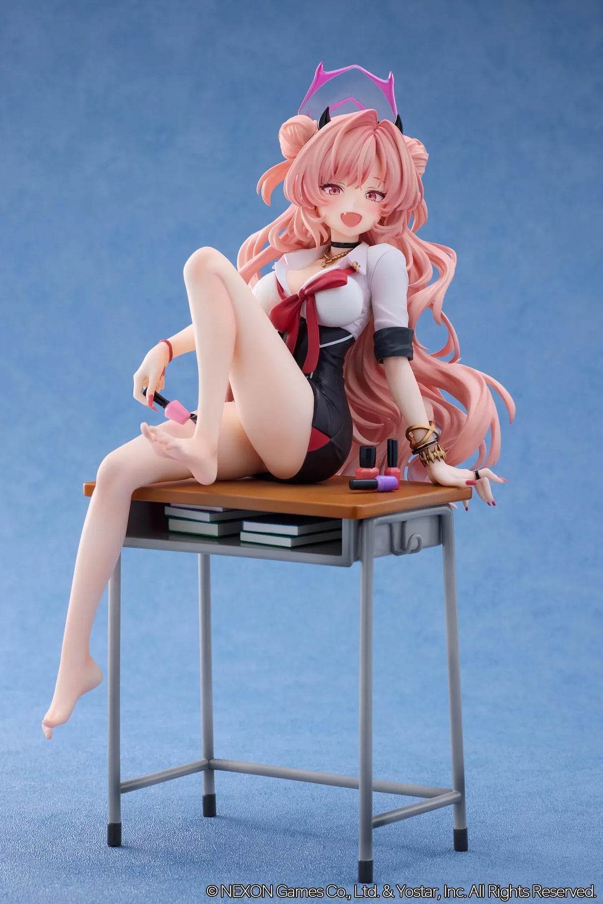 Blue Archive Kirara figure with long pink hair, black horns, and a pink halo, seated on a classroom desk beside nail polish bottles.