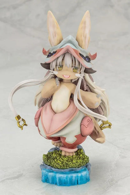 Made in Abyss The Awakening Mystery Nanachi Figure (Rerelease) featuring a fluffy rabbit-like character with long cream-colored ears, golden eyes, an oversized explorer hat, pink and beige clothing, and long flowing hair standing on a detailed scenic base with green moss, rocks, and blue water.