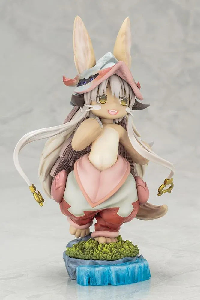 Made in Abyss The Awakening Mystery Nanachi Figure (Rerelease) featuring a fluffy rabbit-like character with long cream-colored ears, golden eyes, an oversized explorer hat, pink and beige clothing, and long flowing hair standing on a detailed scenic base with green moss, rocks, and blue water.