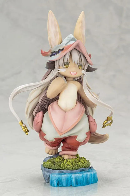 Made in Abyss The Awakening Mystery Nanachi Figure (Rerelease) featuring a fluffy rabbit-like character with long cream-colored ears, golden eyes, an oversized explorer hat, pink and beige clothing, and long flowing hair standing on a detailed scenic base with green moss, rocks, and blue water.