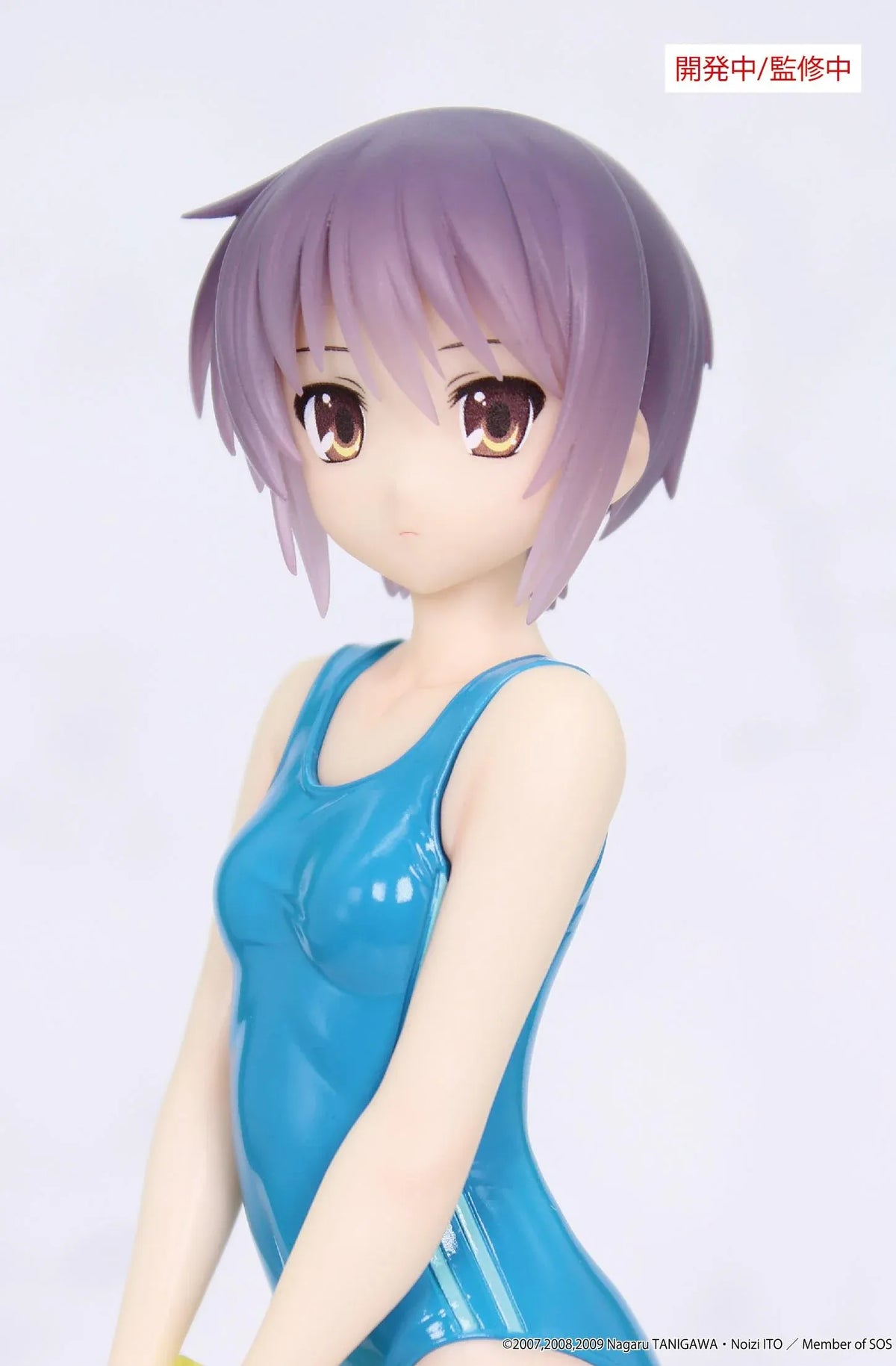 Vivit Yuki Nagato figure with short lavender hair, wearing a blue one-piece swimsuit and holding a yellow book in a crossed-leg standing pose.