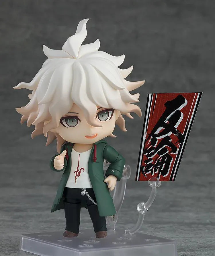 Nendoroid Nagito Komaeda with tousled white hair, pale green eyes, a green coat, white printed shirt, and black trousers, extending one hand.