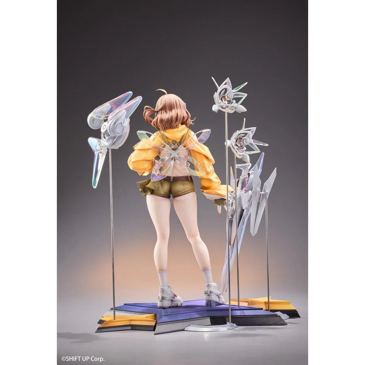 GODDESS OF VICTORY: NIKKE Anis: Star 1/7 Scale Figure featuring a brown-haired anime girl wearing a yellow jacket, white top, olive-green shorts, and sneakers, surrounded by futuristic floating mechanical accessories on a detailed display base.