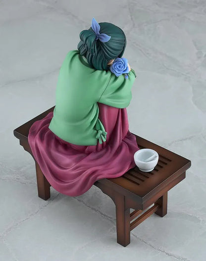 Maomao 1/7 scale figure seated barefoot on a wooden bench, wearing a green top and plum skirt, holding a blue flower beside a mortar and pestle.