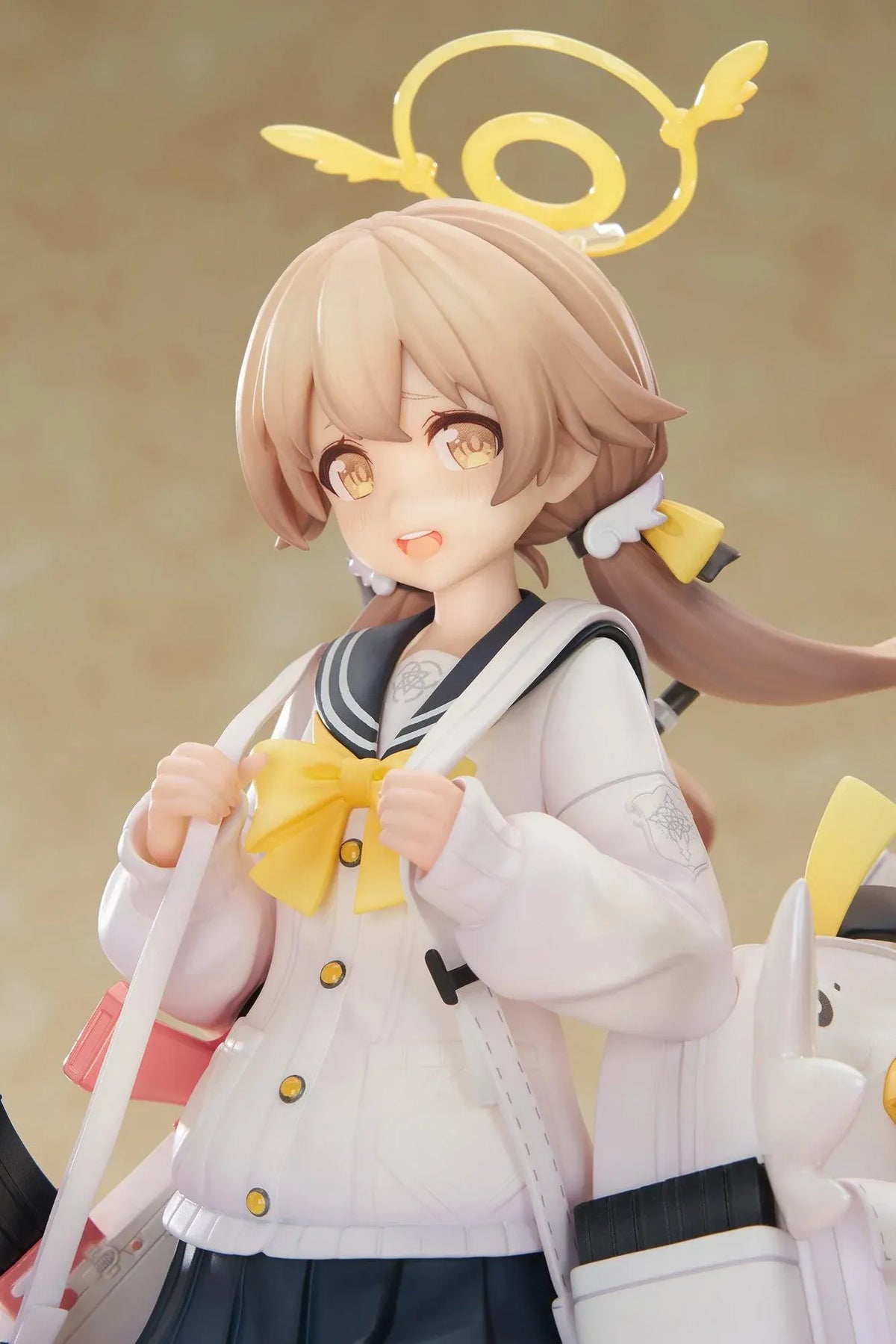 Blue Archive Hifumi figure smiling with one foot lifted, wearing a white cardigan and navy skirt, carrying a bird-themed bag and rifle on a yellow base.