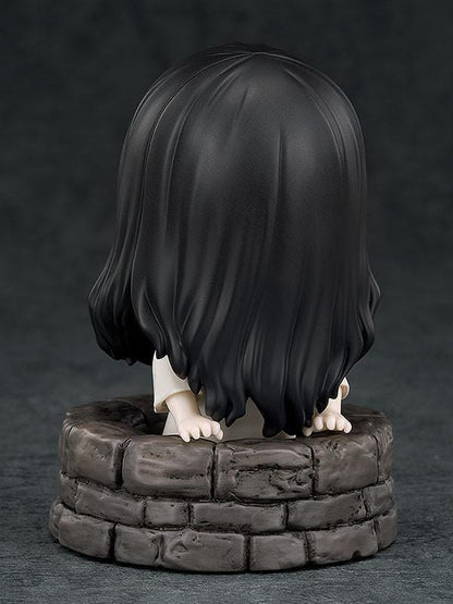 Nendoroid Sadako figure with long black hair covering her face, wearing a white dress and standing barefoot on a clear display base.