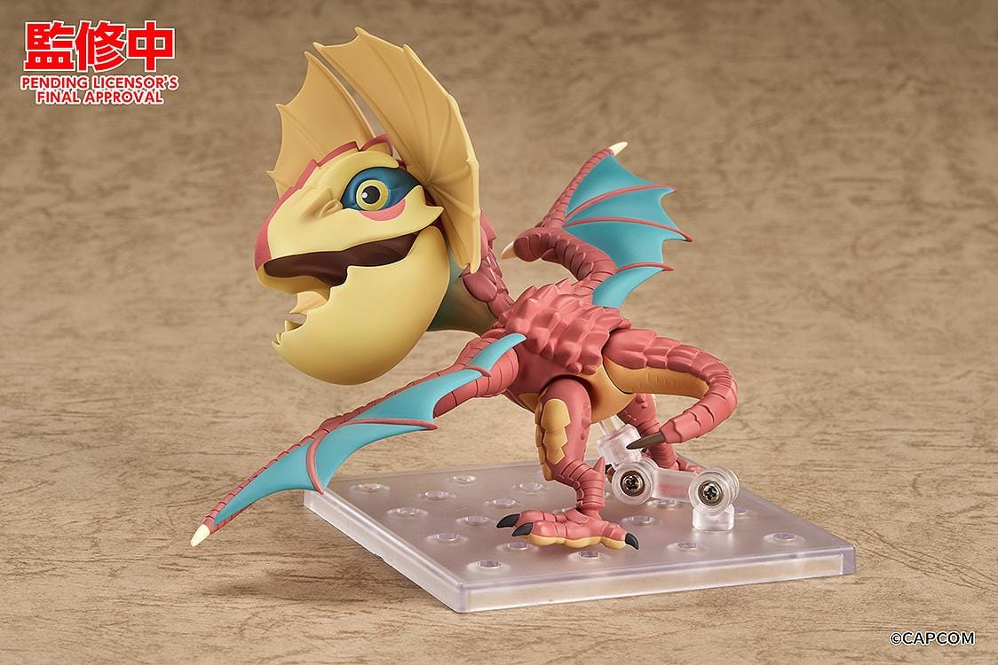 Monster Hunter Nendoroid Yian Kut-Ku with yellow ear fans, an open beak, pink-red scales, and spread wings with turquoise membranes.