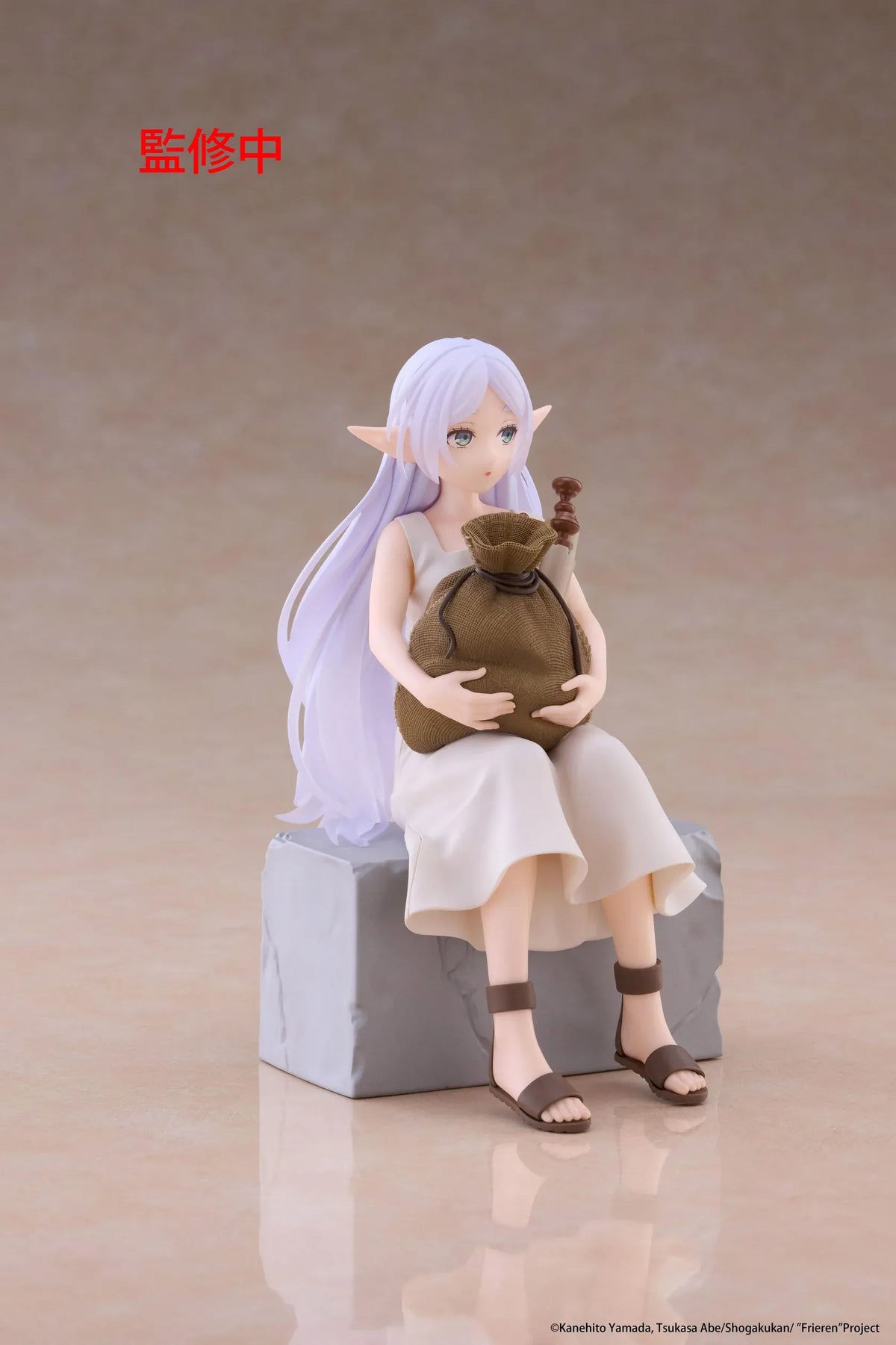 Desktop Cute Frieren In Training Ver. figure seated on a gray stone block, wearing a cream dress and brown sandals while holding a sack beside rolled scrolls.