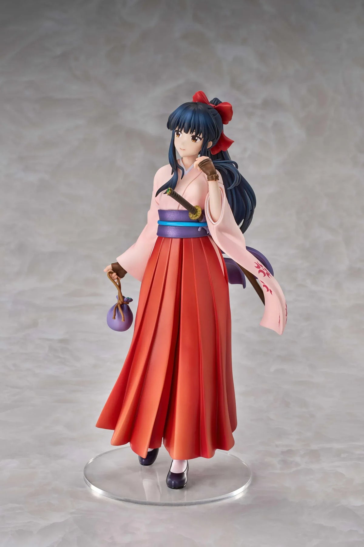 Sakura Wars Sakura Shinguji 1/7 Scale Figure featuring a dark blue-haired anime girl with brown eyes, a red hair ribbon, pink kimono-style top, purple obi, flowing red hakama skirt, sword accessory, and purple pouch on a transparent circular base.