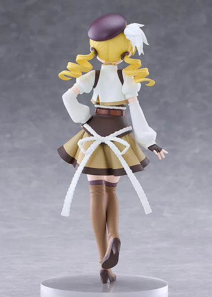 Mami Tomoe figure with blonde spiral curls, a brown hat, white and gold outfit, and tall brown boots, posing with one hand on her hip.