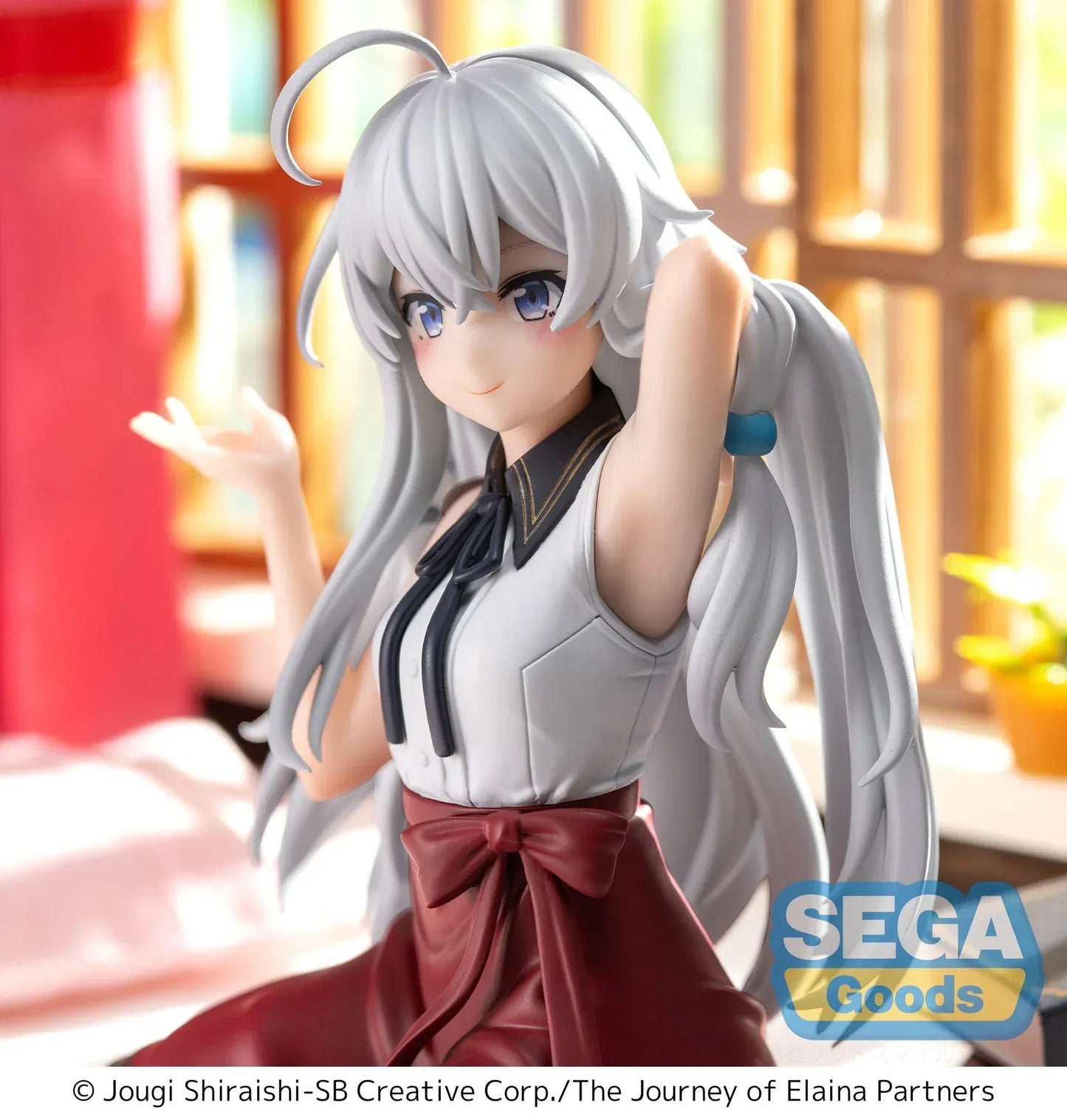 Figure of Elaina from Wandering Witch: The Journey of Elaina sitting on a bed in a white blouse and red skirt, with long silver hair and books beside her, in a sunlit room.