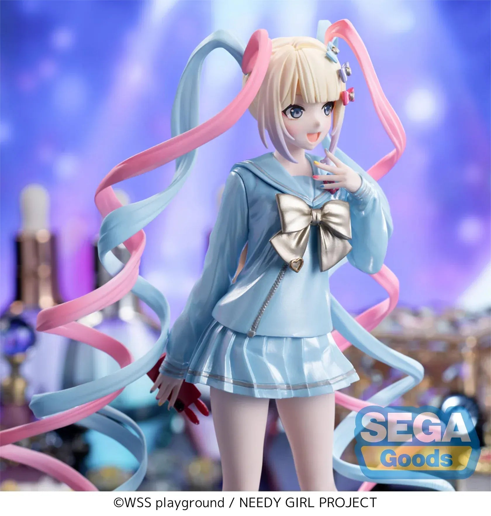 Luminasta OMGKawaiiAngel figure from Needy Streamer Overload standing on a clear base, wearing a pastel blue school outfit with gold bow and long pink-and-blue spiral twin tails, surrounded by makeup and accessories.