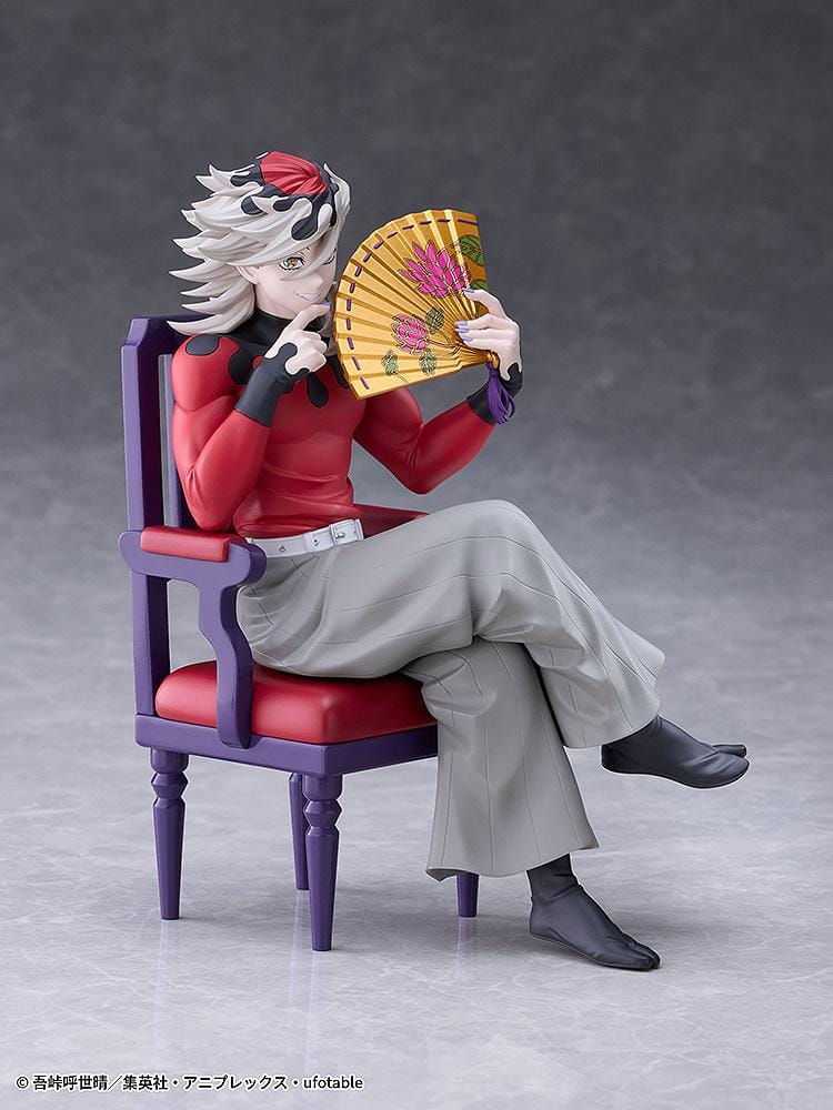 Doma figure seated cross-legged on a purple chair with red cushions, holding a gold floral fan and wearing a red top with gray trousers.