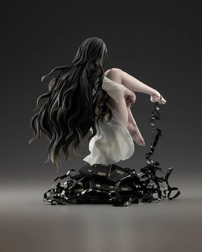 Sadako BISHOUJO Sadako 1/7 Scale Figure (Rerelease) featuring a long black-haired horror character wearing a flowing white dress, seated above a pile of VHS tapes with tangled black film ribbons.