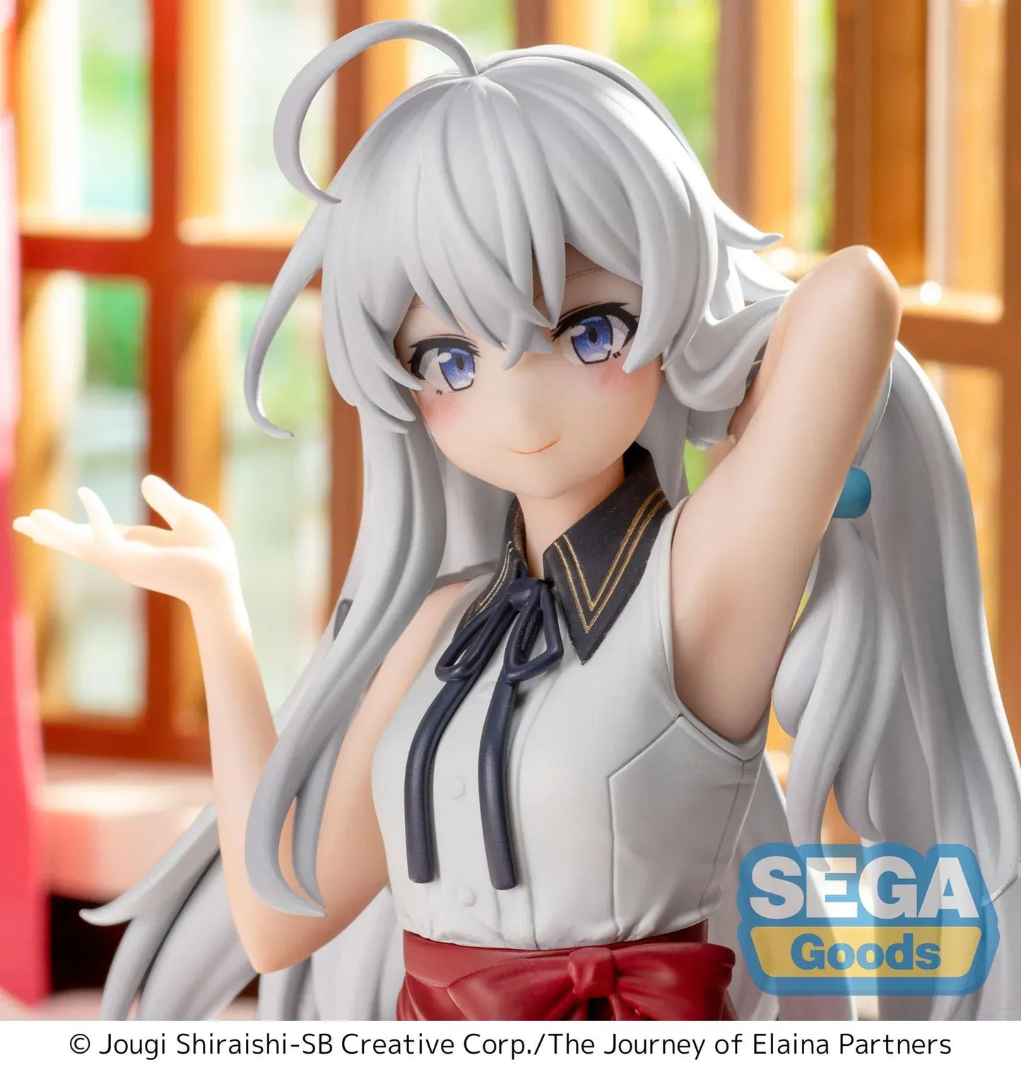 Figure of Elaina from Wandering Witch: The Journey of Elaina sitting on a bed in a white blouse and red skirt, with long silver hair and books beside her, in a sunlit room.