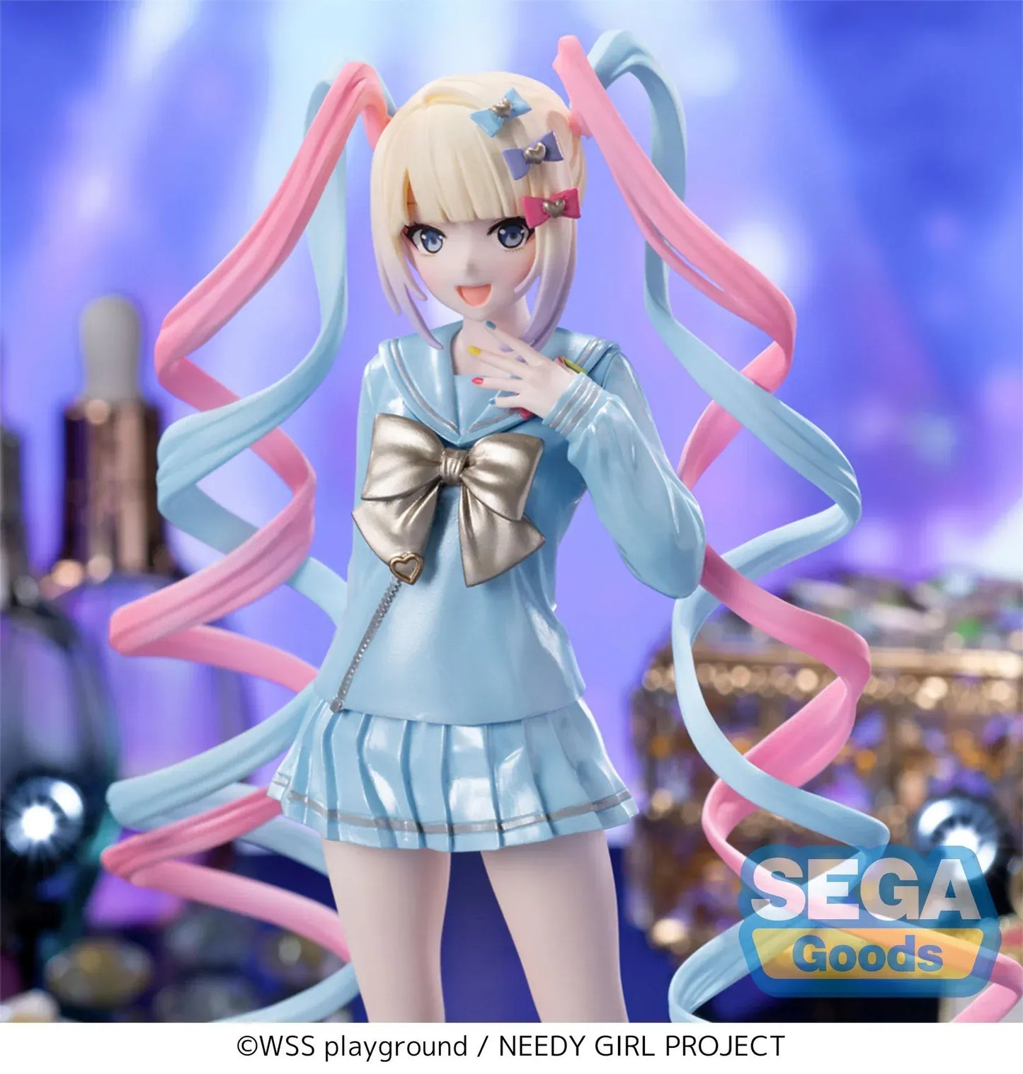 Luminasta OMGKawaiiAngel figure from Needy Streamer Overload standing on a clear base, wearing a pastel blue school outfit with gold bow and long pink-and-blue spiral twin tails, surrounded by makeup and accessories.