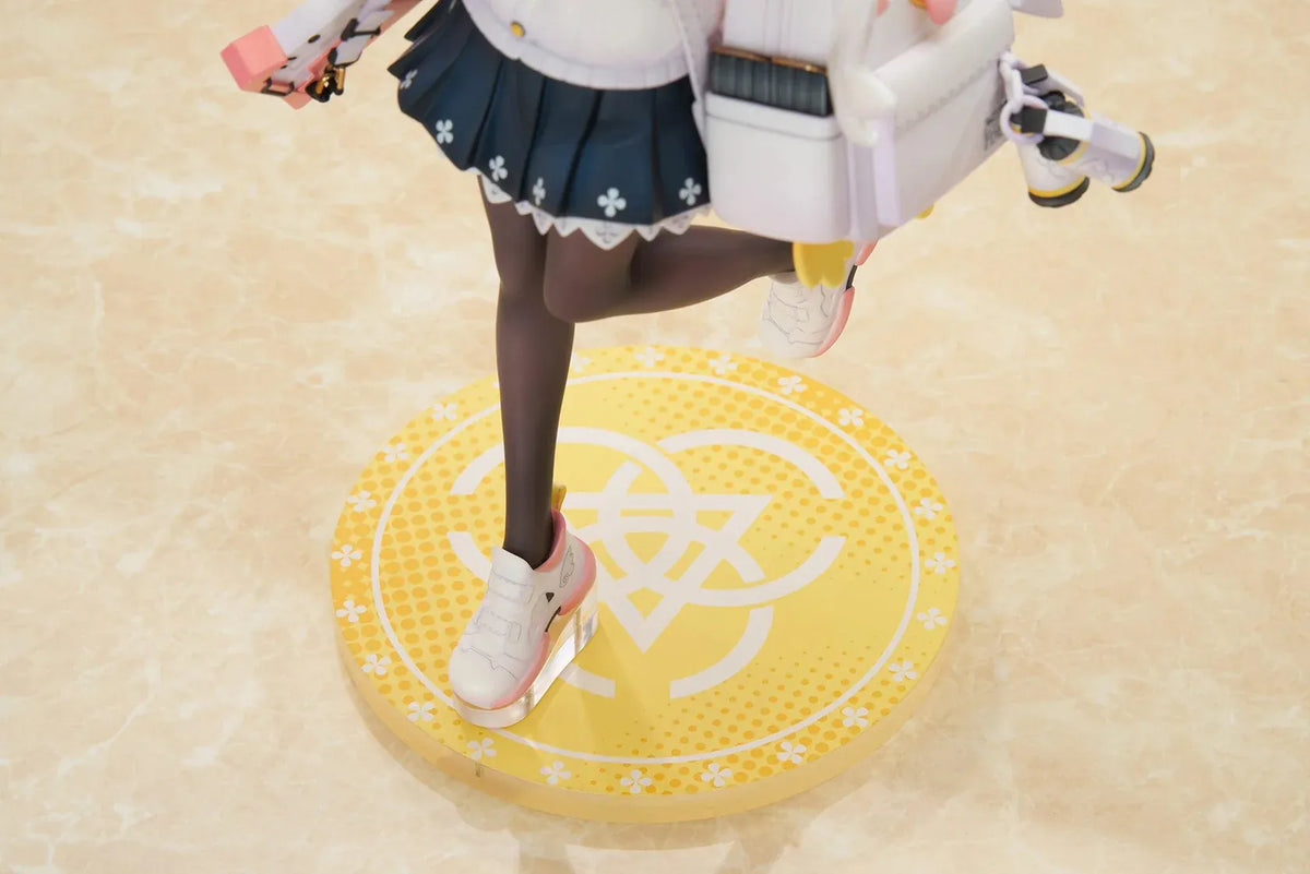 Blue Archive Hifumi figure smiling with one foot lifted, wearing a white cardigan and navy skirt, carrying a bird-themed bag and rifle on a yellow base.