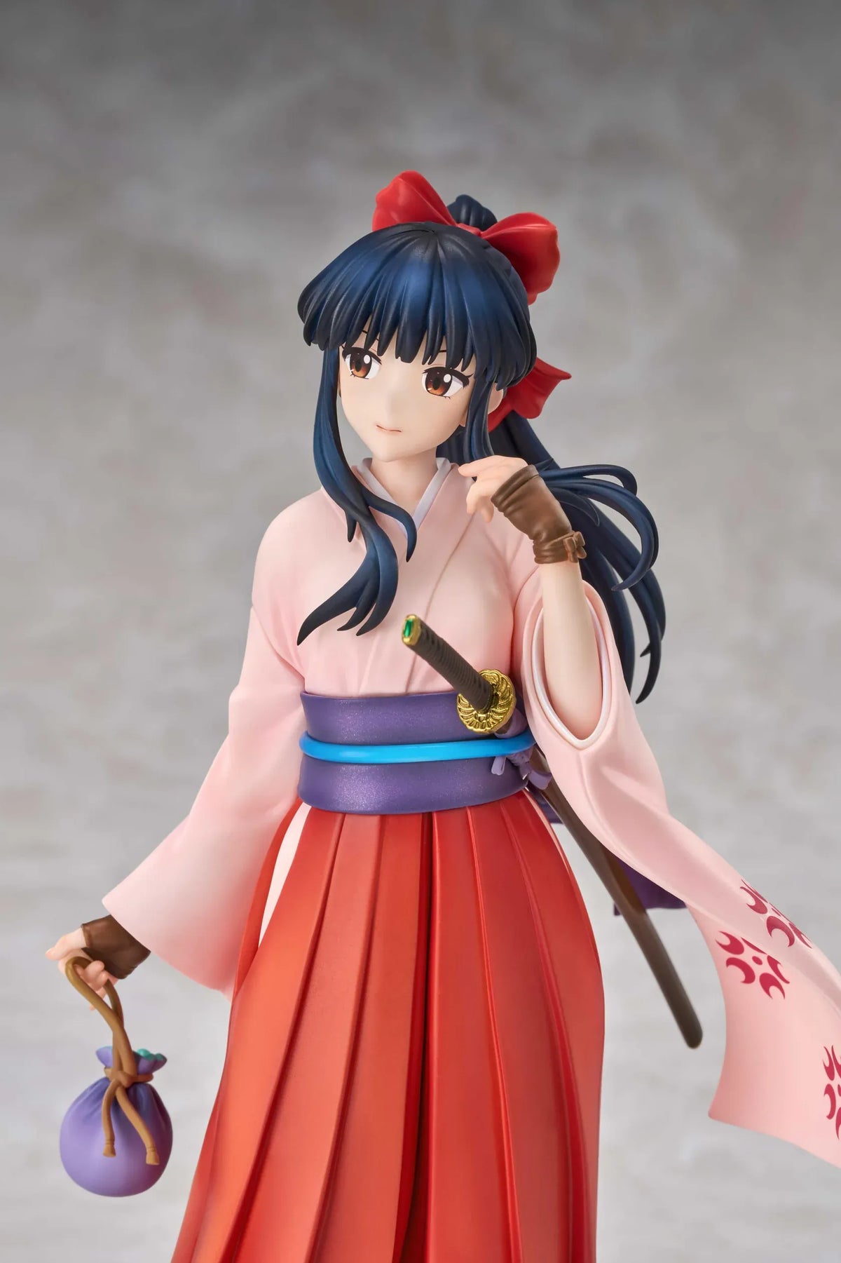 Sakura Wars Sakura Shinguji 1/7 Scale Figure featuring a dark blue-haired anime girl with brown eyes, a red hair ribbon, pink kimono-style top, purple obi, flowing red hakama skirt, sword accessory, and purple pouch on a transparent circular base.