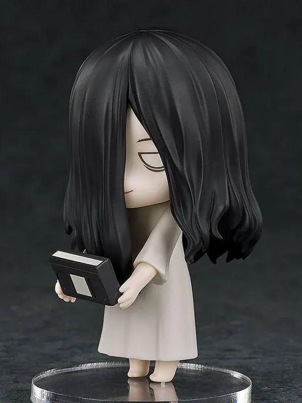 Nendoroid Sadako figure with long black hair covering her face, wearing a white dress and standing barefoot on a clear display base.