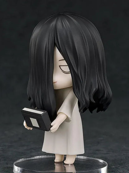 Nendoroid Sadako figure with long black hair covering her face, wearing a white dress and standing barefoot on a clear display base.