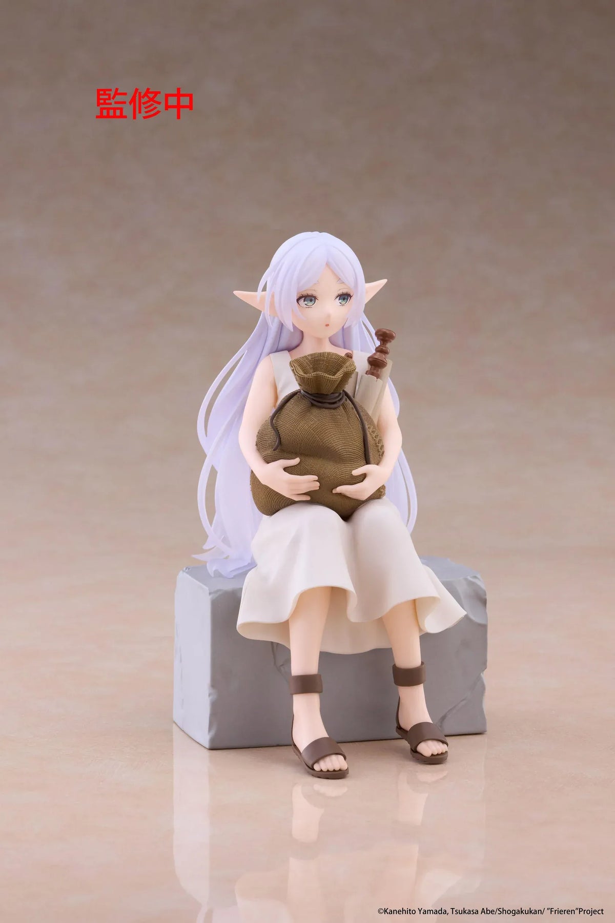 Desktop Cute Frieren In Training Ver. figure seated on a gray stone block, wearing a cream dress and brown sandals while holding a sack beside rolled scrolls.
