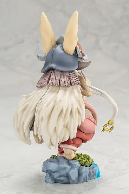 Made in Abyss The Awakening Mystery Nanachi Figure (Rerelease) featuring a fluffy rabbit-like character with long cream-colored ears, golden eyes, an oversized explorer hat, pink and beige clothing, and long flowing hair standing on a detailed scenic base with green moss, rocks, and blue water.