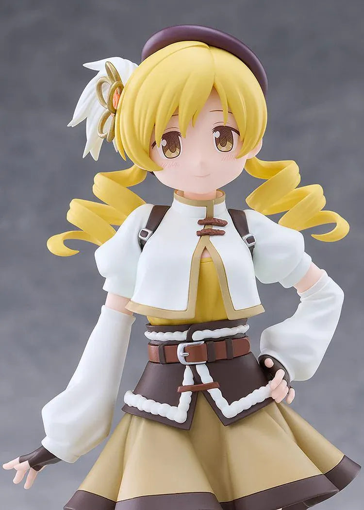 Mami Tomoe figure with blonde spiral curls, a brown hat, white and gold outfit, and tall brown boots, posing with one hand on her hip.