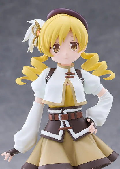Mami Tomoe figure with blonde spiral curls, a brown hat, white and gold outfit, and tall brown boots, posing with one hand on her hip.