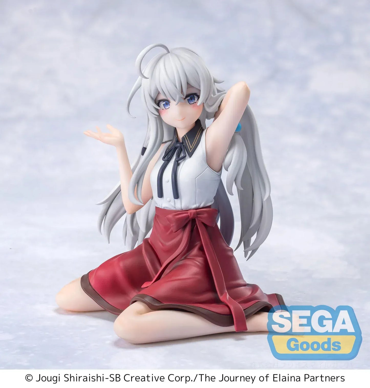 Figure of Elaina from Wandering Witch: The Journey of Elaina sitting on a bed in a white blouse and red skirt, with long silver hair and books beside her, in a sunlit room.
