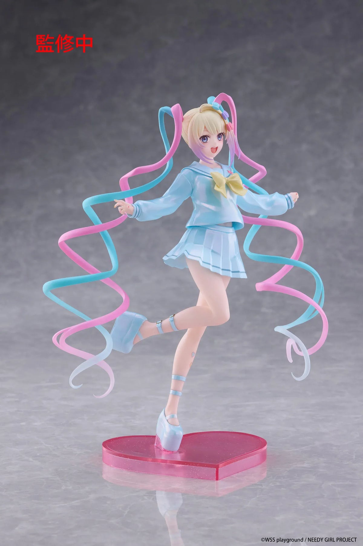 Needy Girl Overdose OMGKawaiiAngel Coreful Figure featuring a blonde-haired anime girl with blue eyes, long pink and blue twin-tails, a pastel-blue sailor-style outfit, yellow bow, and matching shoes posed on a pink heart-shaped base.