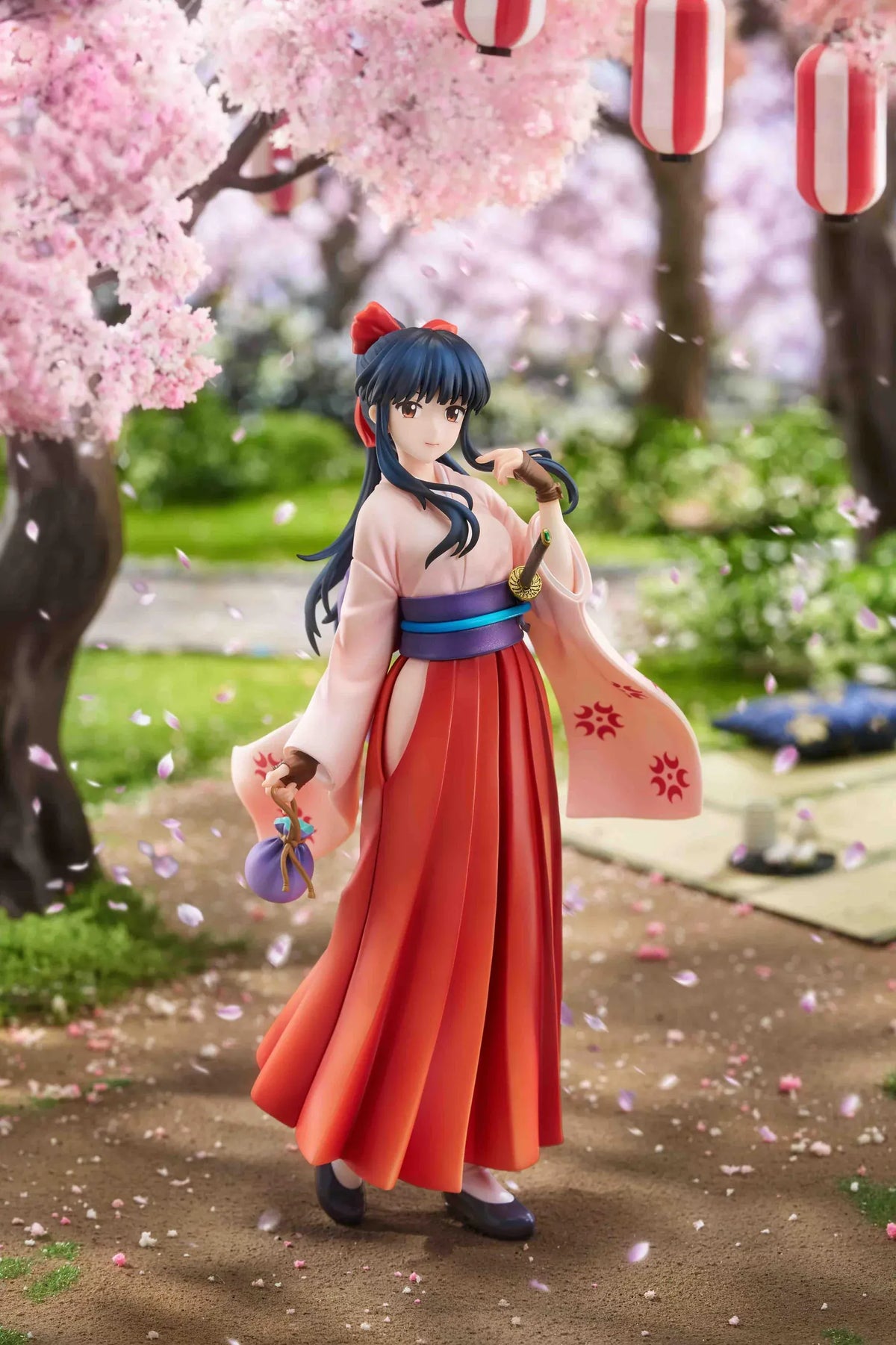 Sakura Wars Sakura Shinguji 1/7 Scale Figure featuring a dark blue-haired anime girl with brown eyes, a red hair ribbon, pink kimono-style top, purple obi, flowing red hakama skirt, sword accessory, and purple pouch on a transparent circular base.