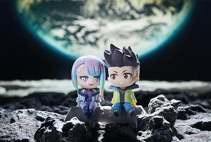 Cyberpunk: Edgerunners Qset+ David & Lucy To The Moon Figure (Rerelease) featuring chibi-style David Martinez with spiky black hair and a yellow jacket sitting beside Lucy Kushinada with pastel-colored hair and a purple futuristic outfit on a shared display base.