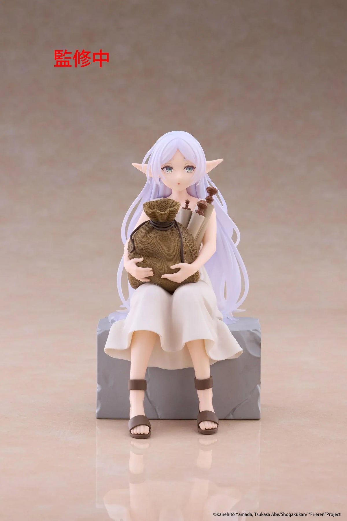 Desktop Cute Frieren In Training Ver. figure seated on a gray stone block, wearing a cream dress and brown sandals while holding a sack beside rolled scrolls.