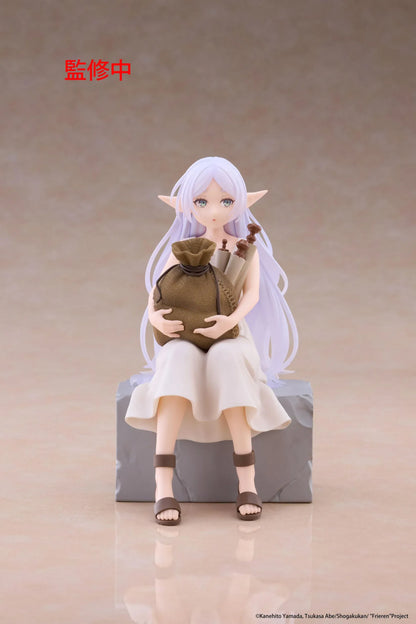 Desktop Cute Frieren In Training Ver. figure seated on a gray stone block, wearing a cream dress and brown sandals while holding a sack beside rolled scrolls.