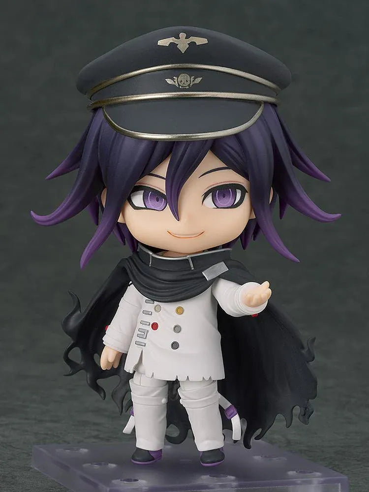 Nendoroid Kokichi Oma with purple hair, violet eyes, a black peaked cap and cape, and a white outfit, smiling with both arms extended.