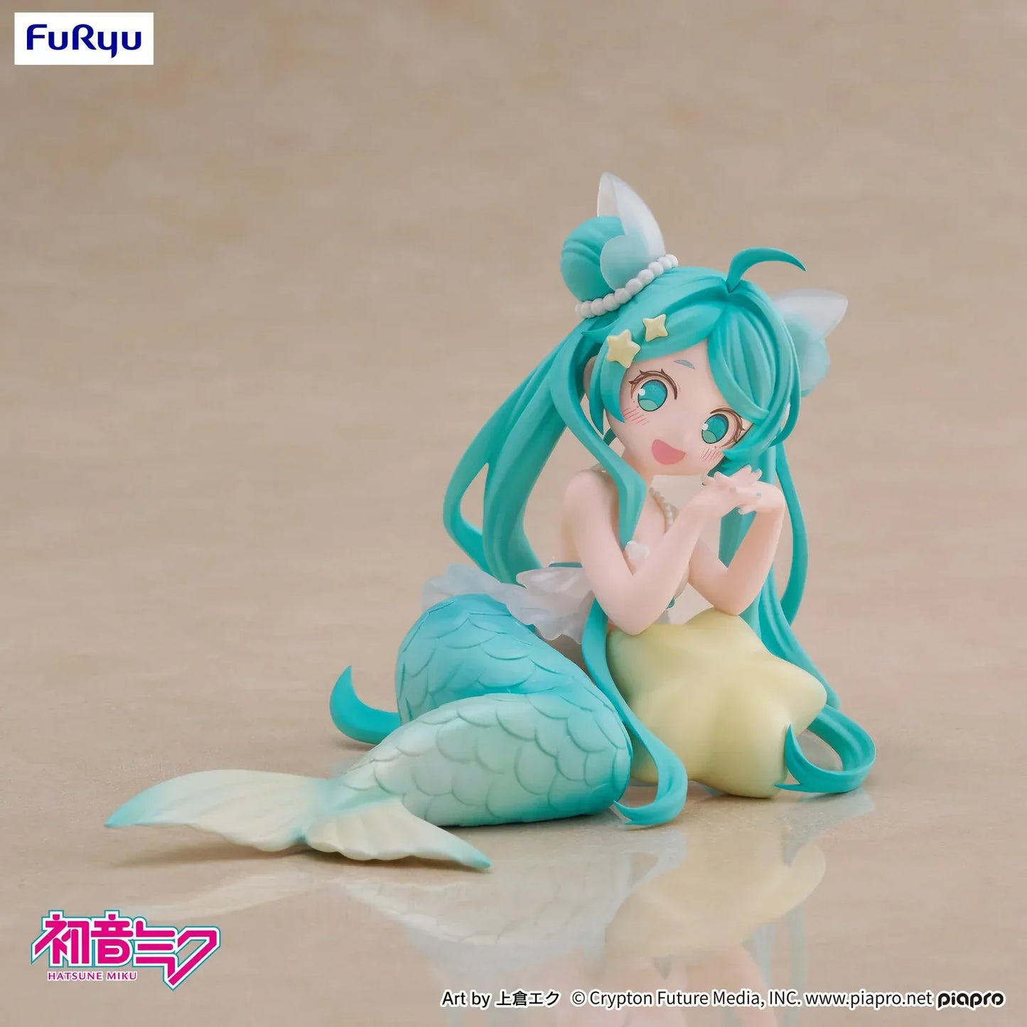 Pastel mermaid Hatsune Miku desktop fairy figure lounging on a star cushion with a mint-green tail and twin-tails, displayed on a desk with seashells and a keyboard in the background.